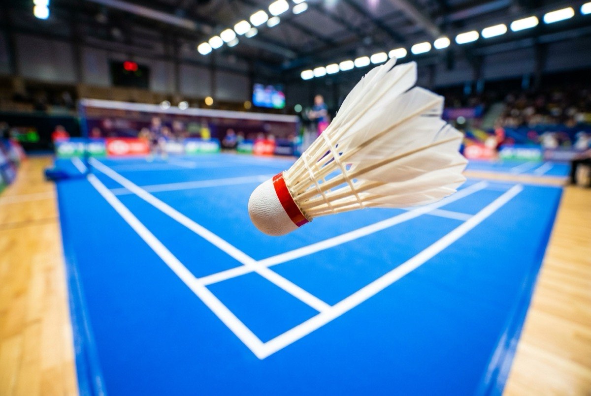Feather shuttlecock suspended mid-flight above a bright blue tournament court