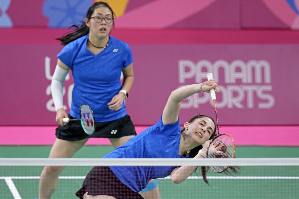 Player playing a low backhand shot while her partner covers