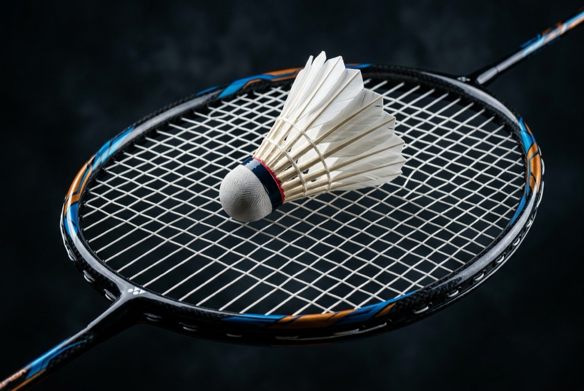 Modern carbon-fibre badminton racket with feather shuttlecock resting on strings, dark studio background